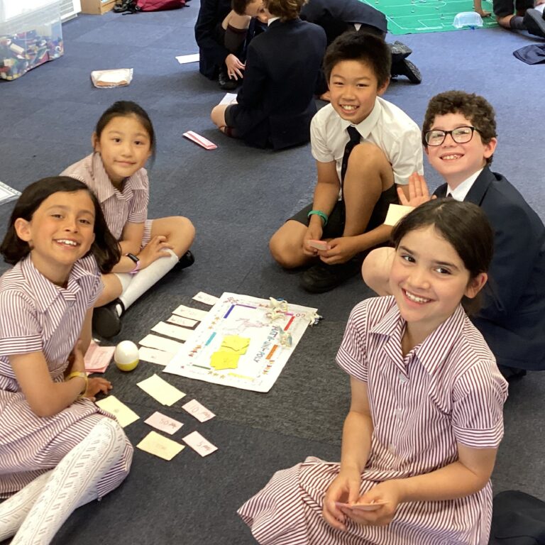 a group of young students sitting on the carpet around a piece of schoolwork