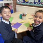 two pre-prep children writing on coloured card